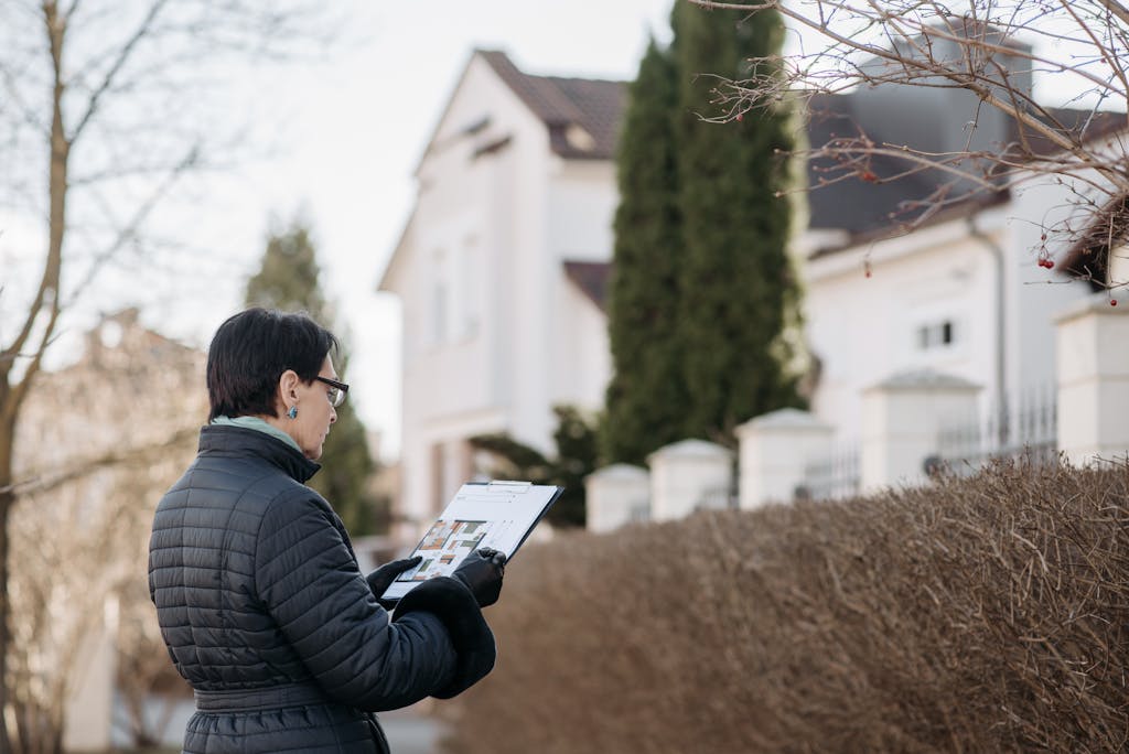 A Woman Standing on the Street while Holding a House Plan - areas to invest in property