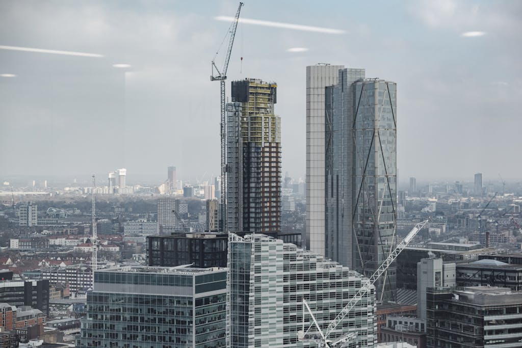 Complex of modern multistory buildings and commercial skyscrapers with tower cranes under cloudy sky in London - areas to invest in property